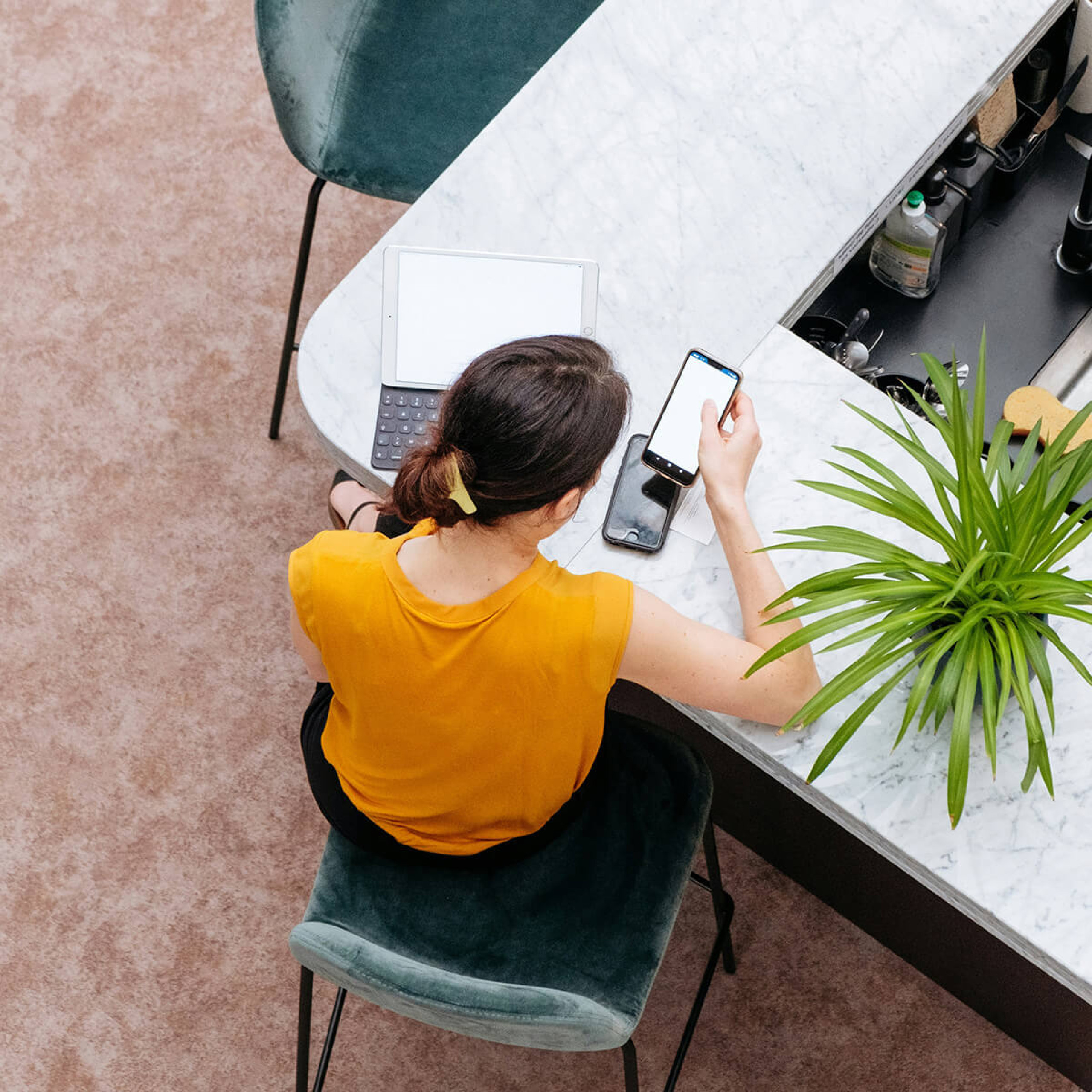 Luftbild einer Frau, die im Coworking Bereich des Greenhouse Senden an einem Tisch sitzt und einen Laptop und ein Smartphone vor sich liegen hat.