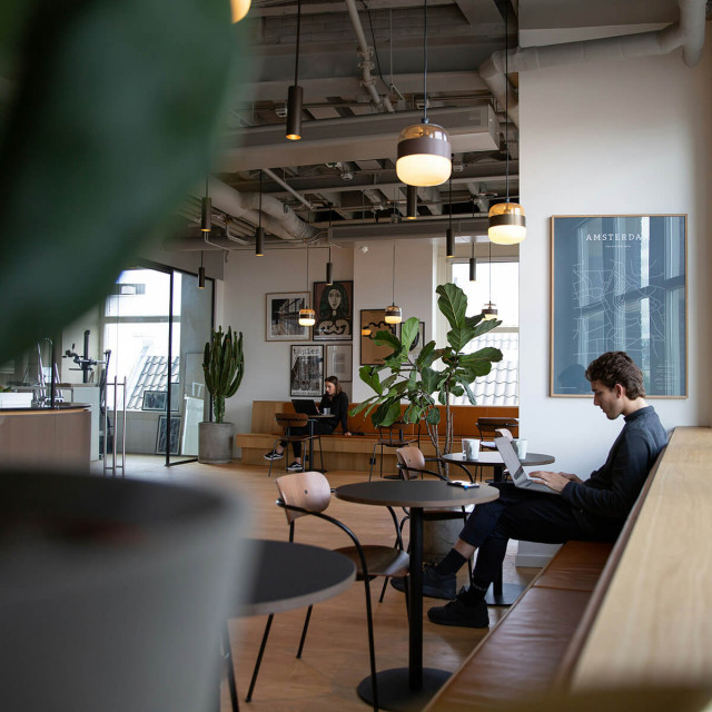 Zwei Personen sitzen in einem modernen Coworking Space an jeweils einem Tisch und arbeiten am Laptop..